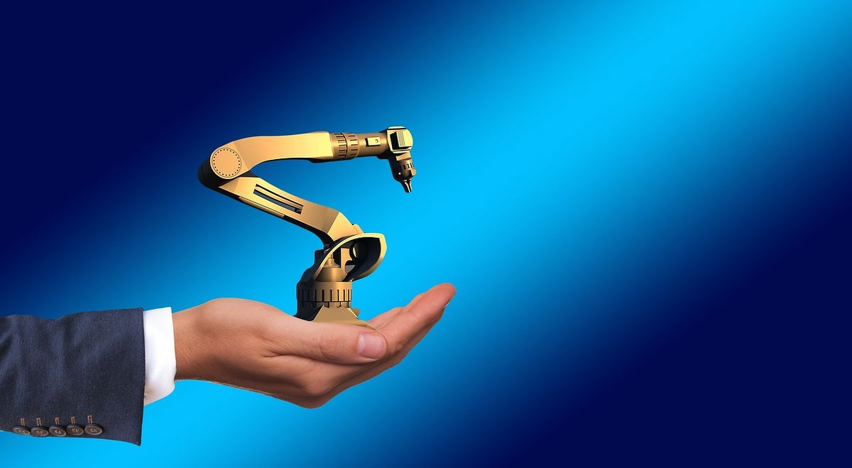 Hand holding a tiny robotic arm against a blue background