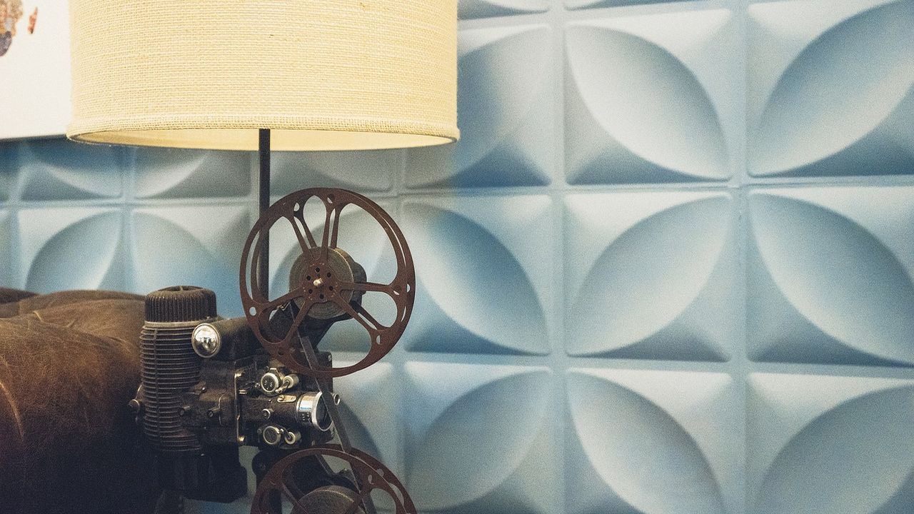 Vintage film projector beside a lamp against a patterned wall