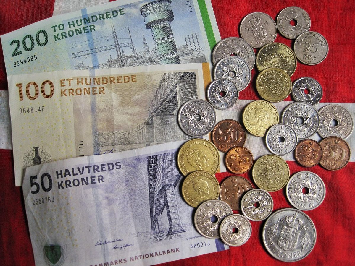 Danish kroner banknotes and coins spread on a red cloth