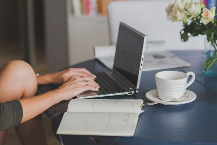 Woman typing on a laptop at a desk with a coffee cup and open notebook
