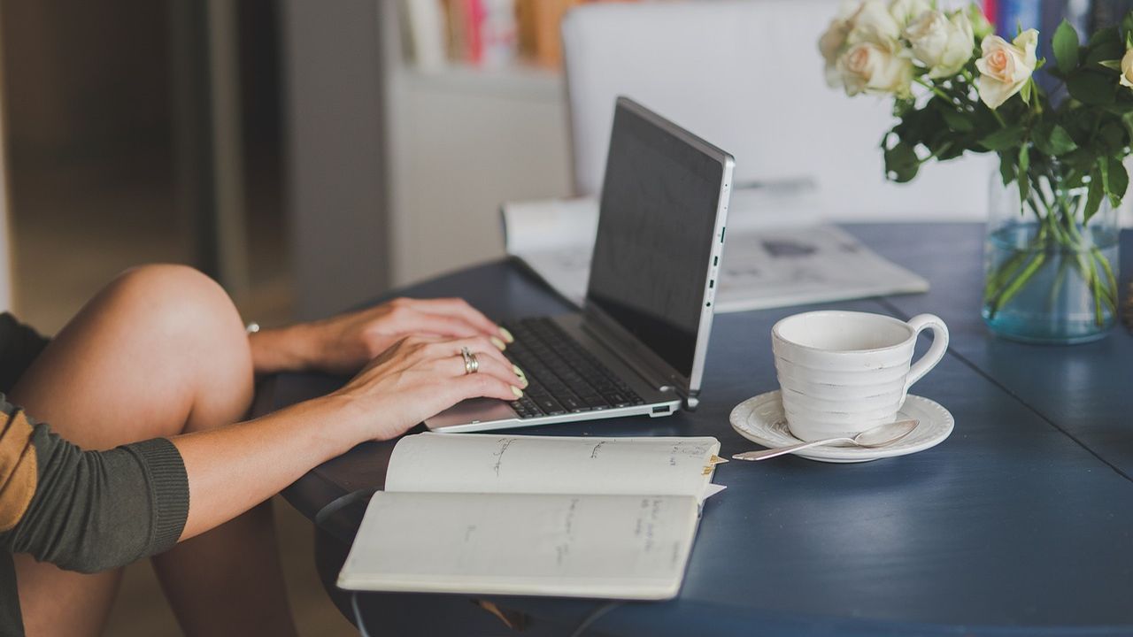 Woman typing on a laptop at a desk with a coffee cup and open notebook