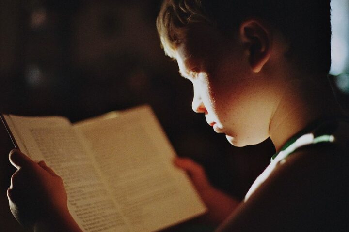 Child reading a book by lamplight