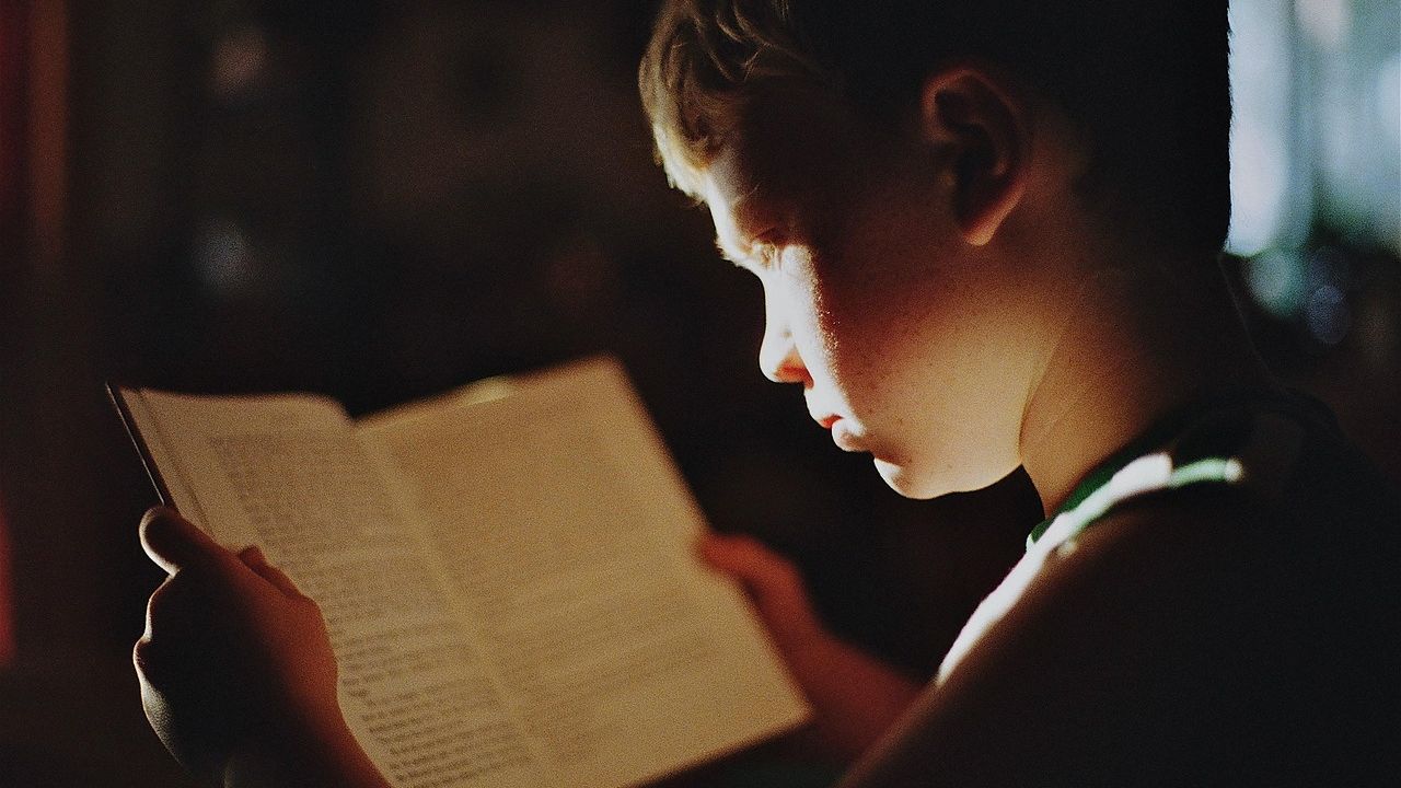 Child reading a book by lamplight