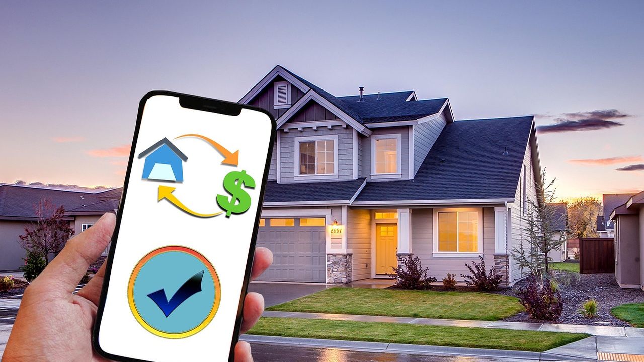 Hand holding a phone with a property finance app in front of a house