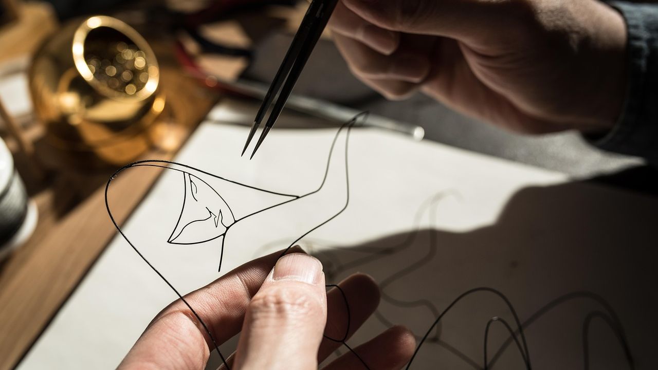 Hands shaping wire with pliers to make jewellery
