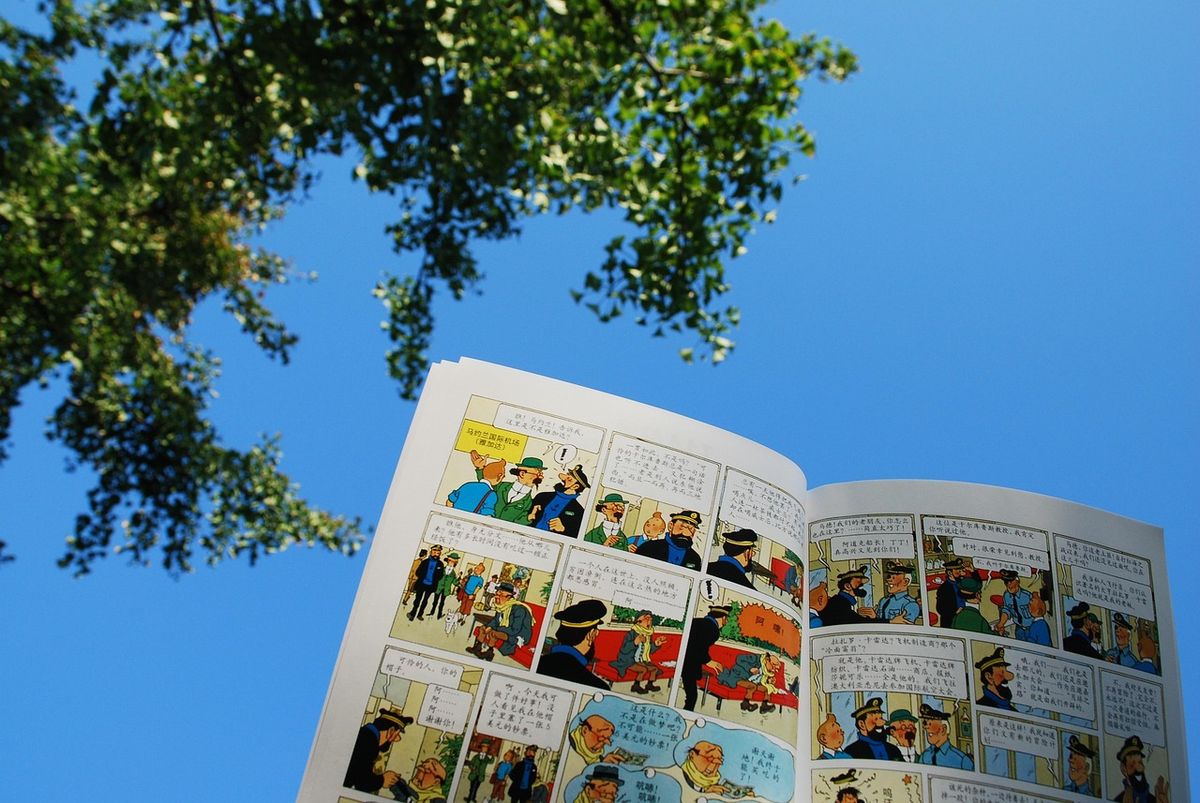 Open comic book held up against a blue sky and trees