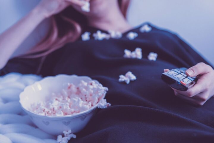Woman on a sofa with a TV remote and a bowl of popcorn