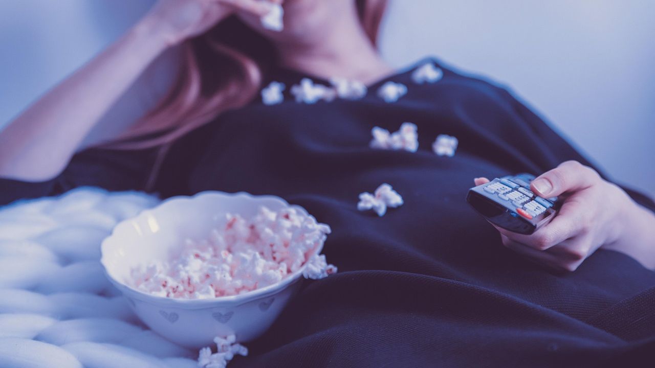 Woman on a sofa with a TV remote and a bowl of popcorn