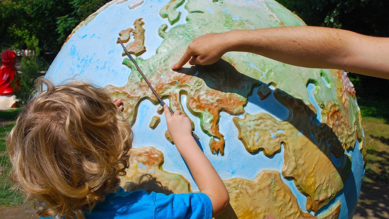 Child and adult pointing at Europe on a large globe