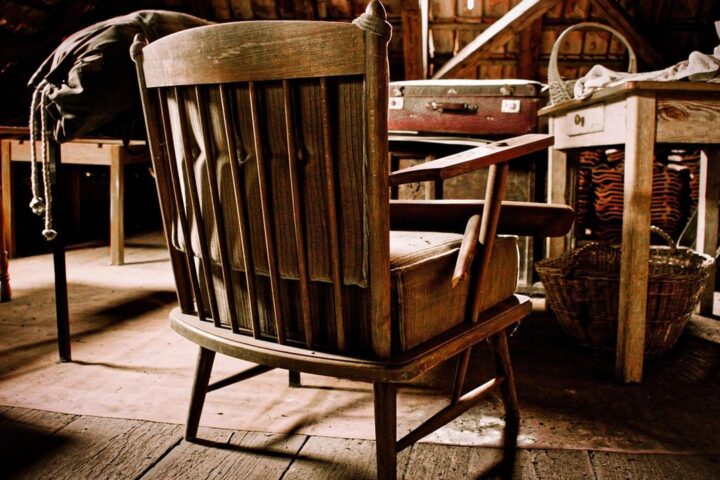 Old wooden chair among antiques in a cluttered barn loft