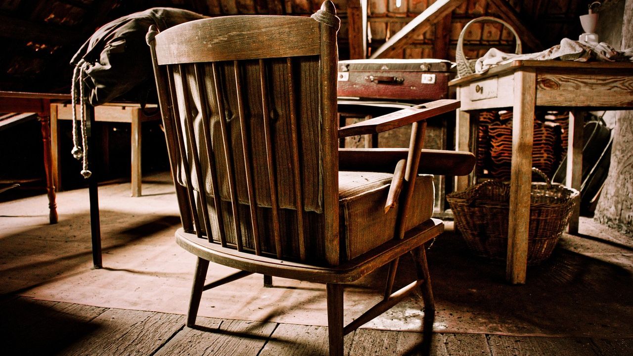 Old wooden chair among antiques in a cluttered barn loft