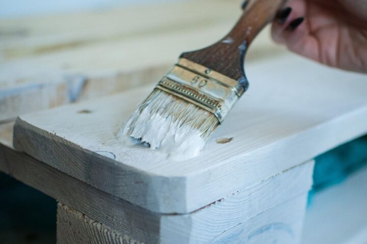 Paintbrush applying white paint to an old wooden pallet