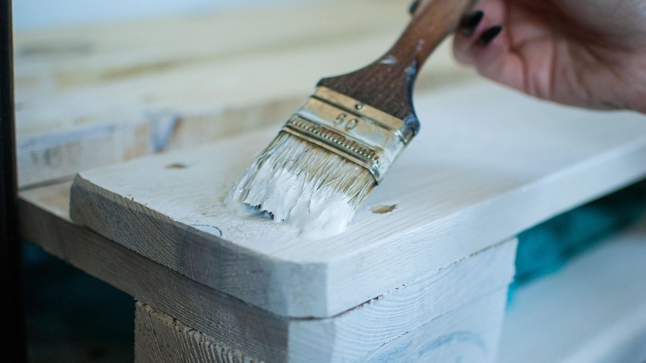 Paintbrush applying white paint to an old wooden pallet
