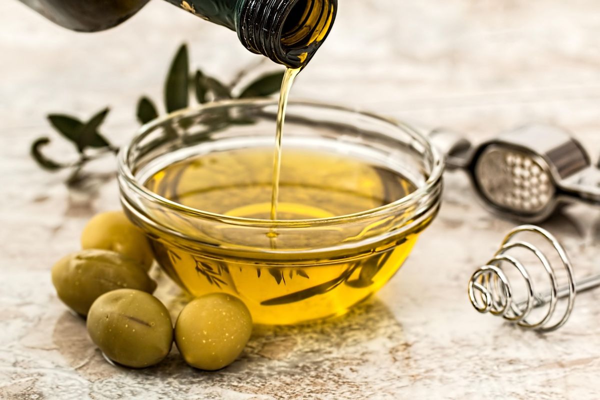 Olive oil being poured into a glass bowl beside olives