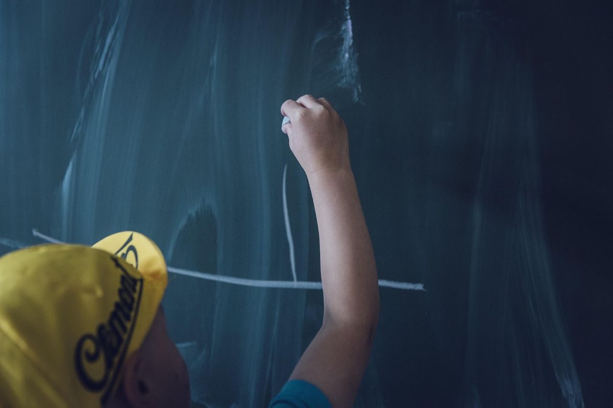 Child reaching up to write on a blackboard