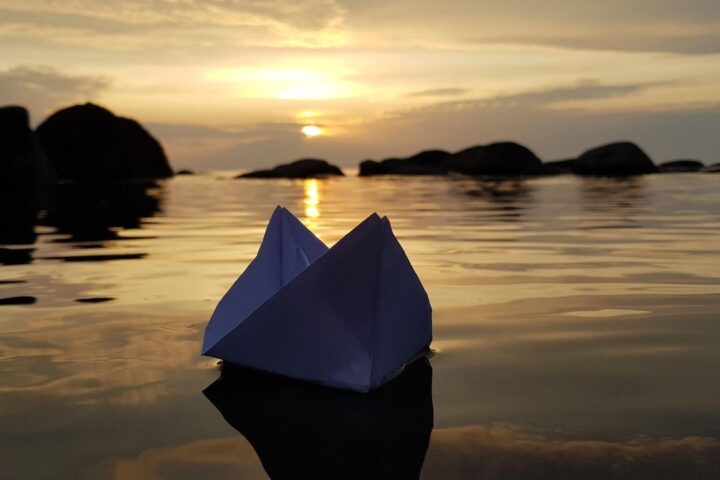 Paper boat floating on calm water at sunset