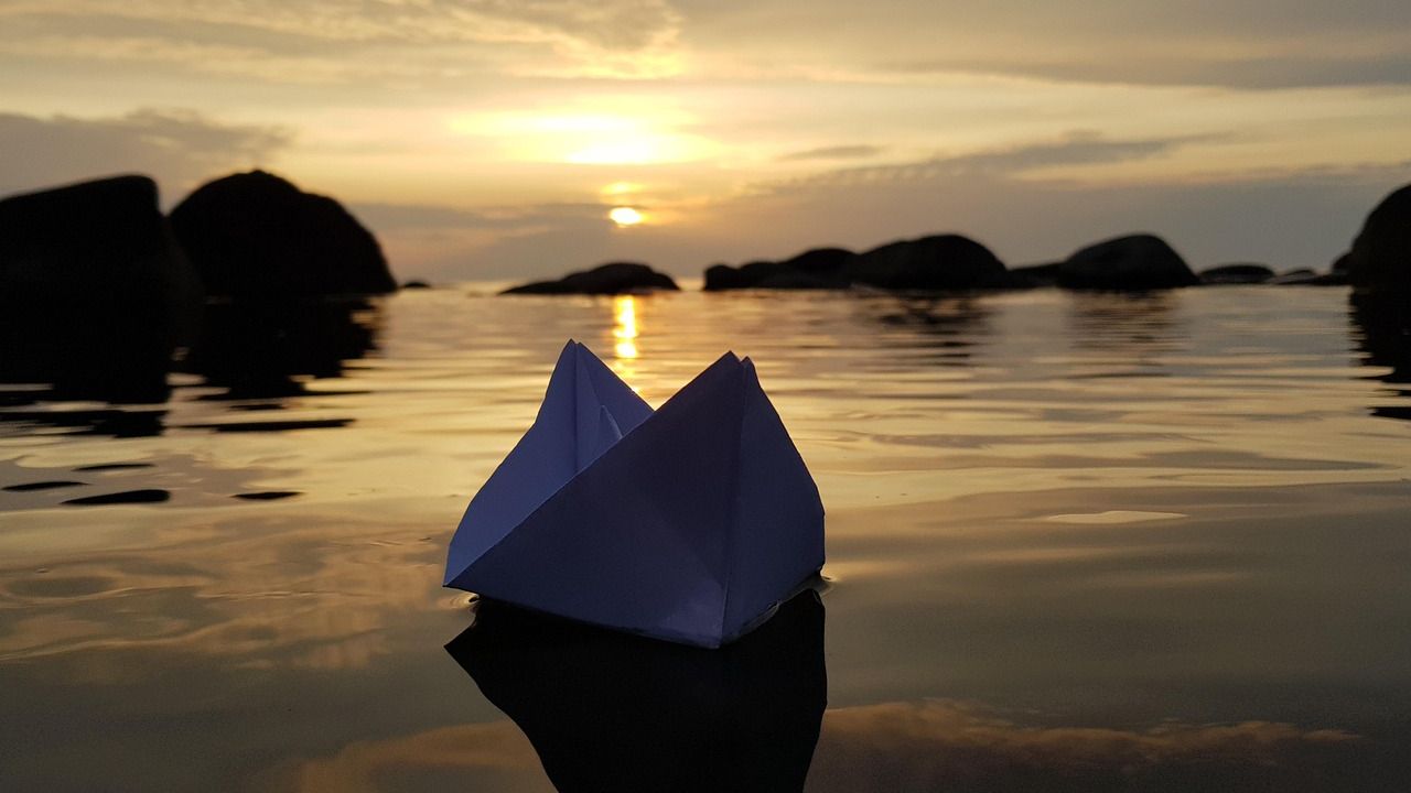 Paper boat floating on calm water at sunset