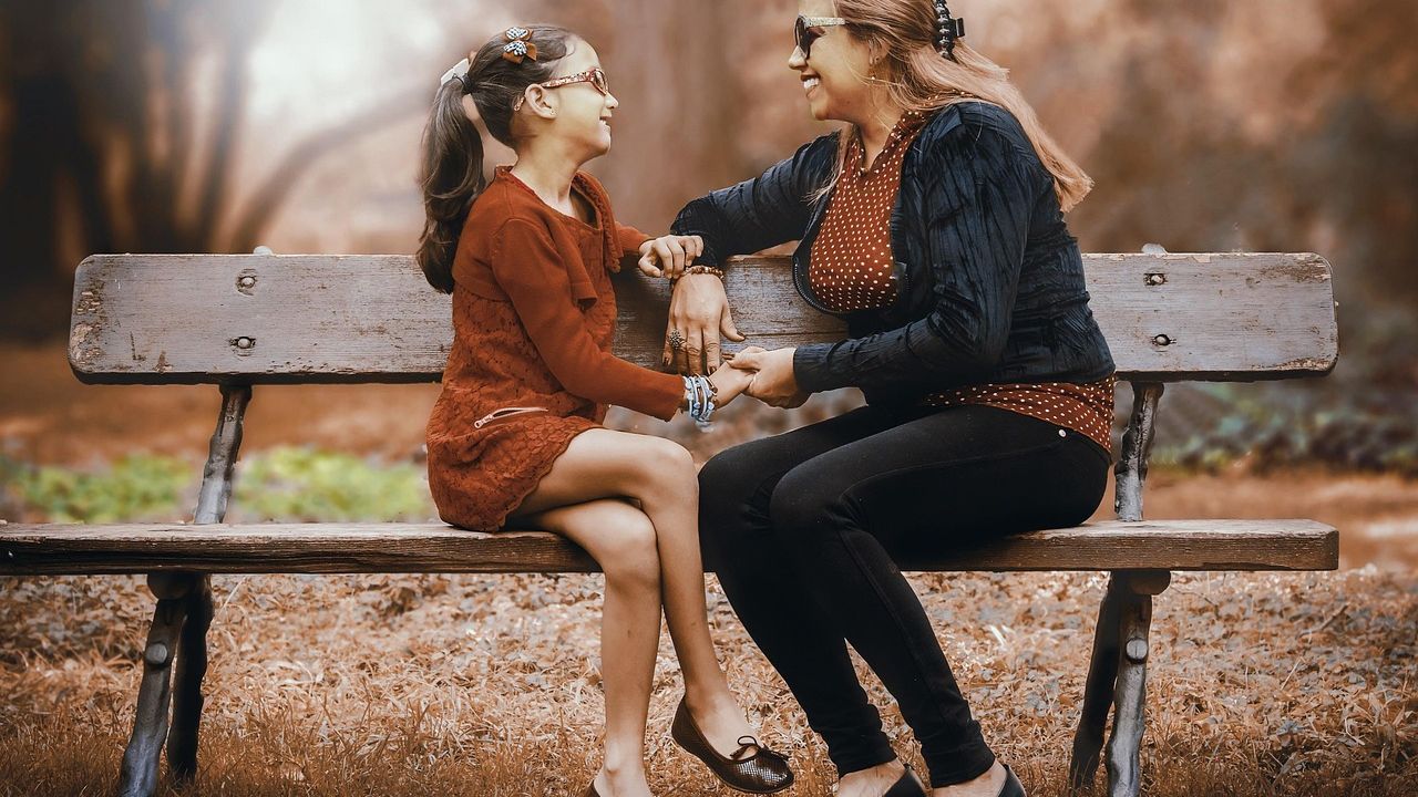 Woman and girl talking on a park bench