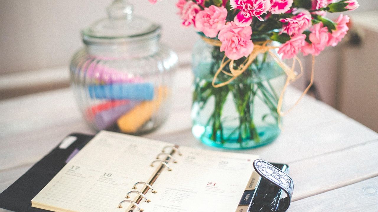 Open planner, pen and flowers on a desk