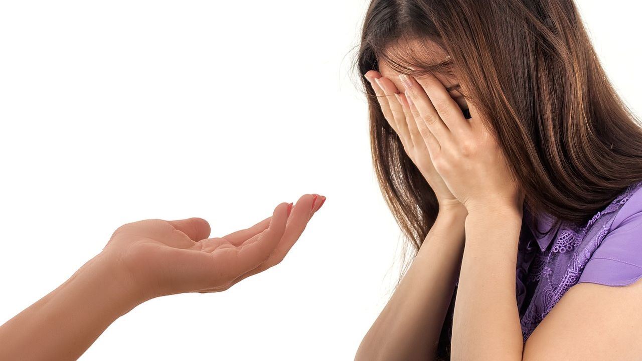 Hand reaching out to a woman with her face in her hands