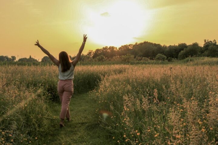 Woman with arms raised walking through a meadow at sunset