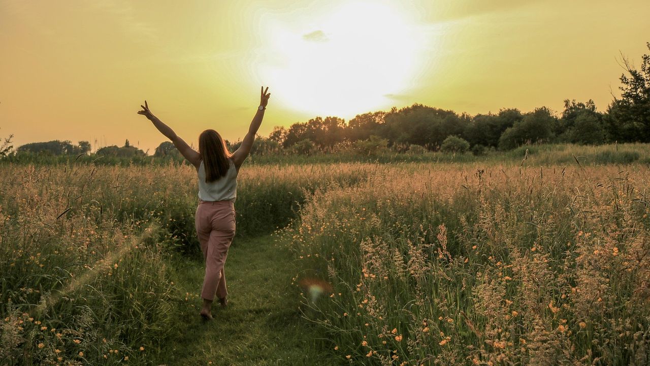Woman with arms raised walking through a meadow at sunset