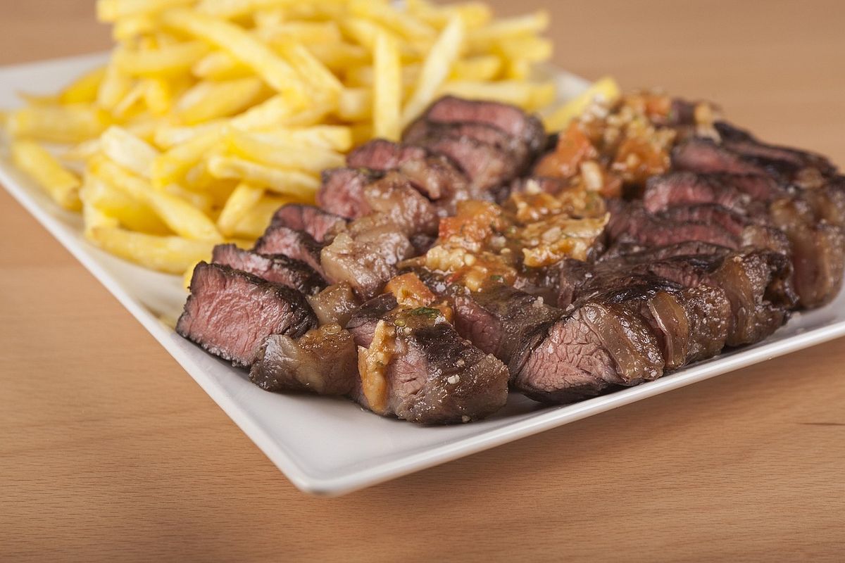 Sliced steak with chips on a white plate