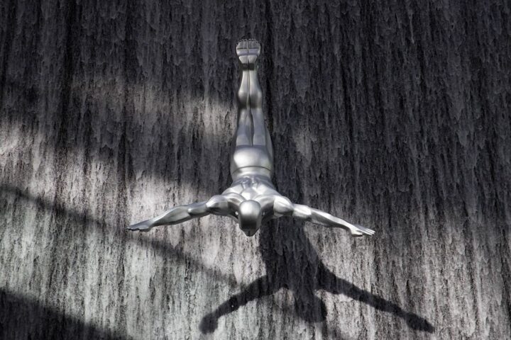 Metal sculpture of a diving figure on a wooden wall