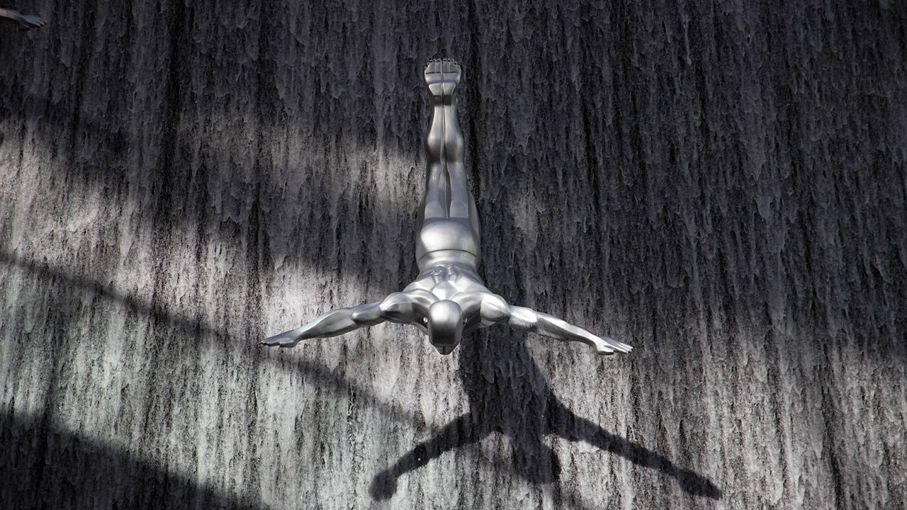 Metal sculpture of a diving figure on a wooden wall