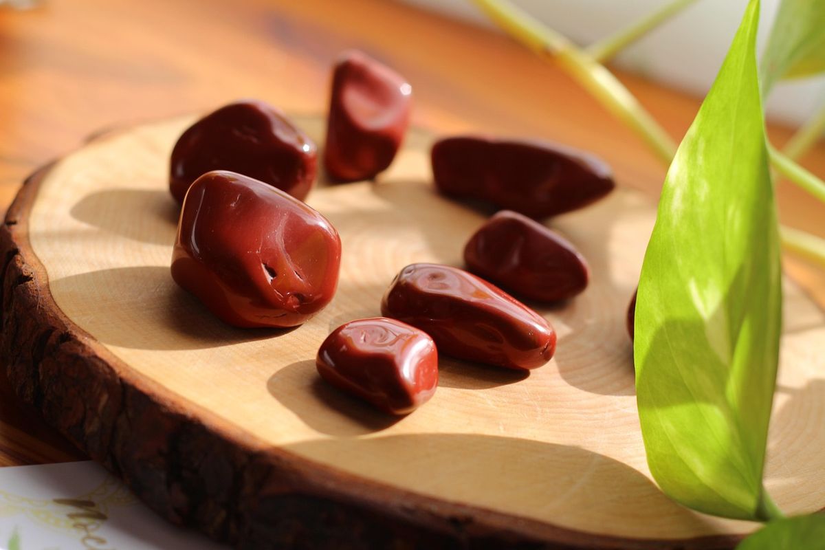 Red jasper stones on a wooden slice beside a green leaf