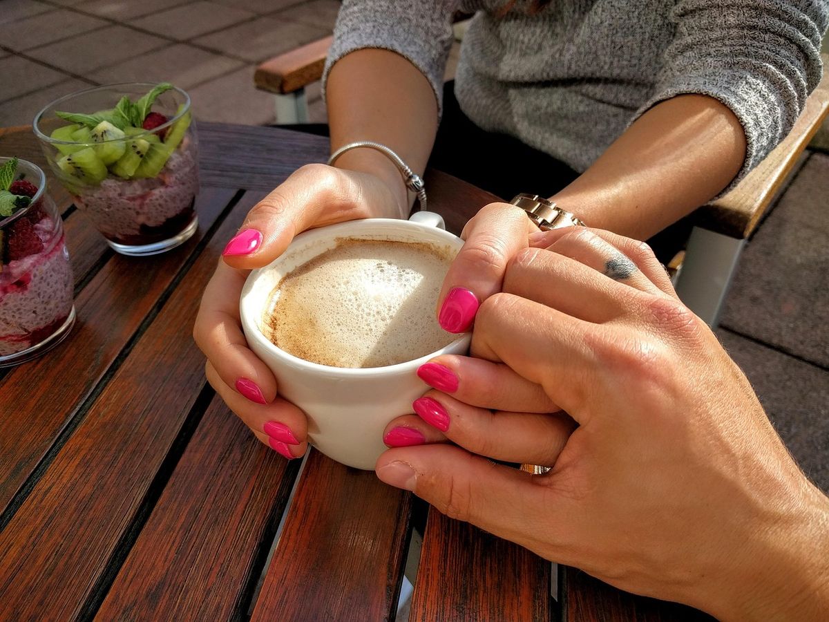 Woman's hands cupping a cappuccino on a café table
