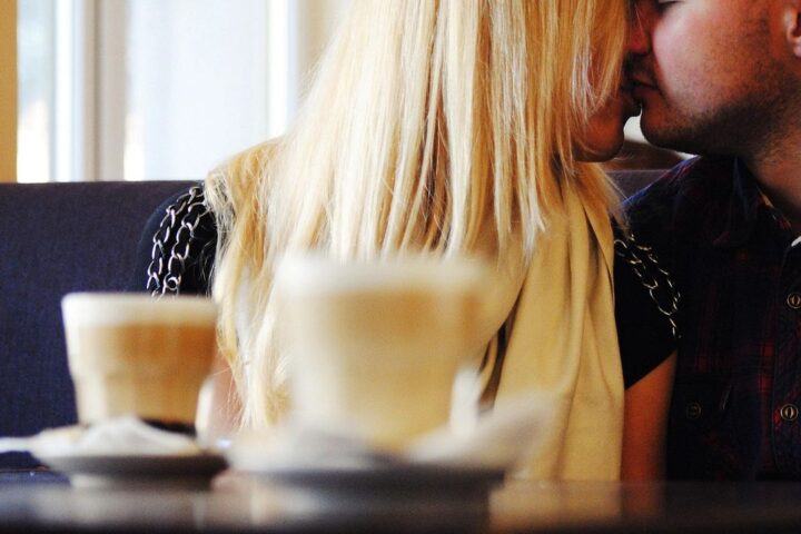 Couple sharing a kiss over cappuccinos in a café