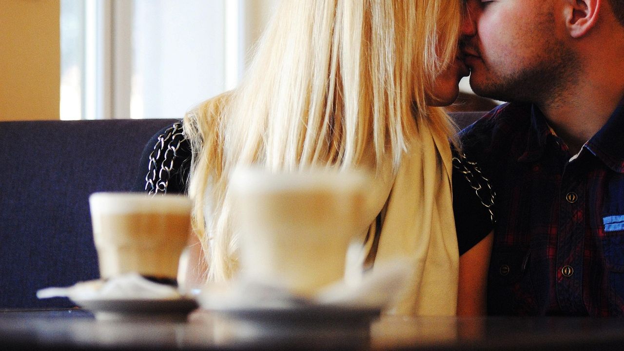 Couple sharing a kiss over cappuccinos in a café