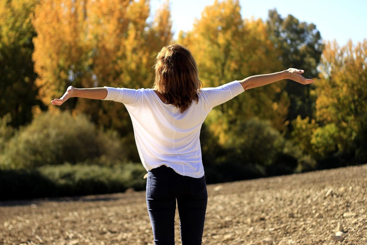 Woman with arms outstretched among autumn trees