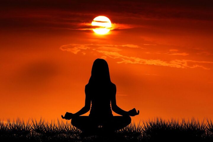 Silhouette of a woman meditating in the lotus position at sunrise