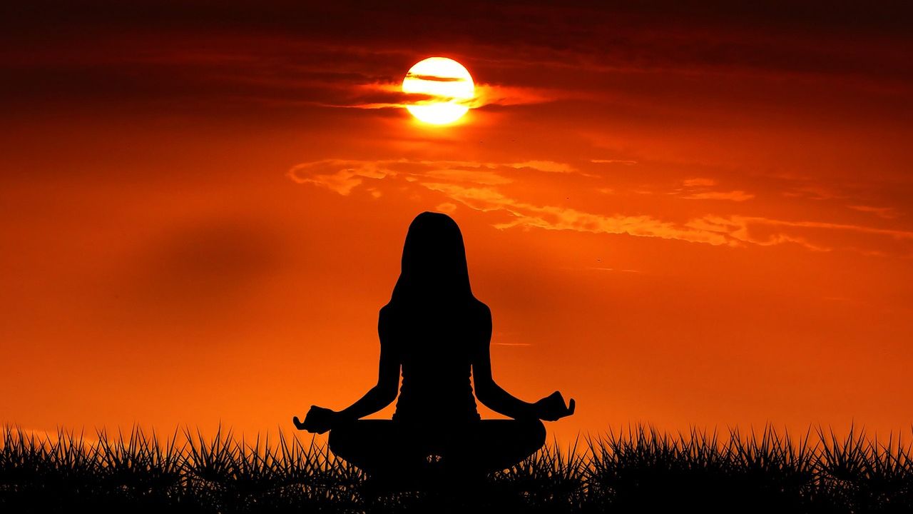 Silhouette of a woman meditating in the lotus position at sunrise