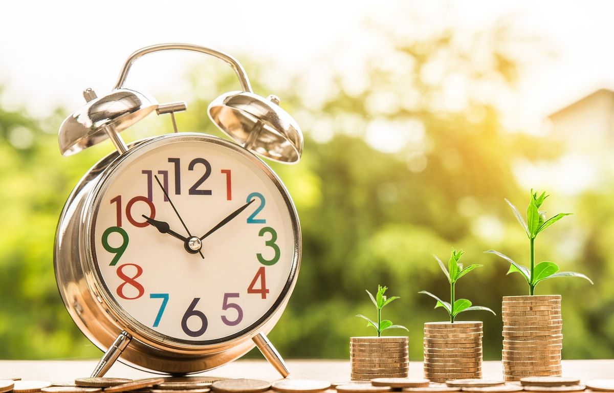 Alarm clock beside coins with seedlings growing