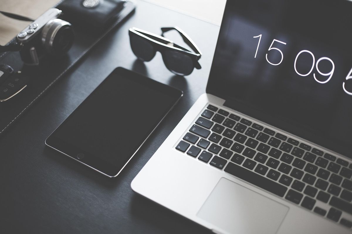 Laptop, tablet and sunglasses on a dark desk