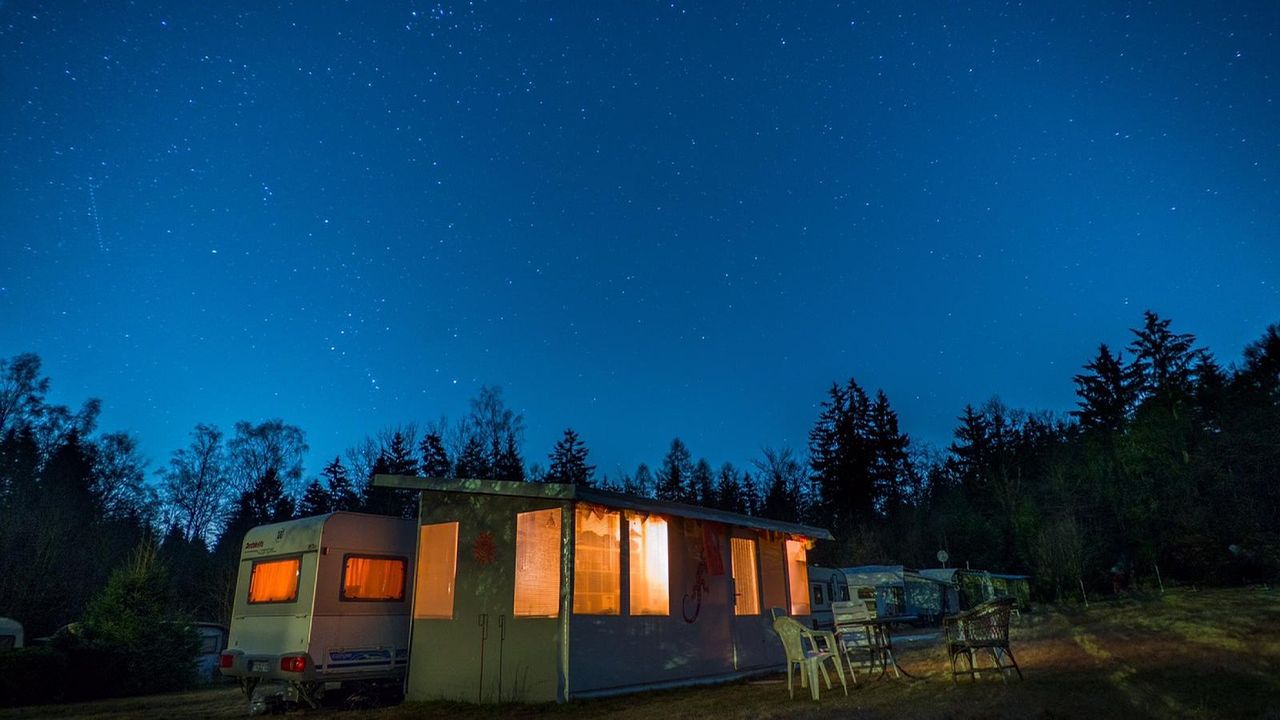 Caravan with glowing windows under a starry night sky