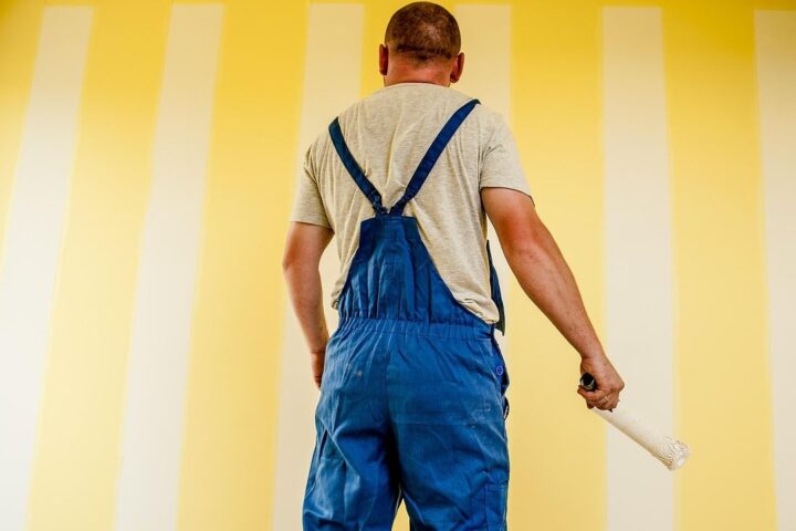Decorator in overalls painting a yellow striped wall
