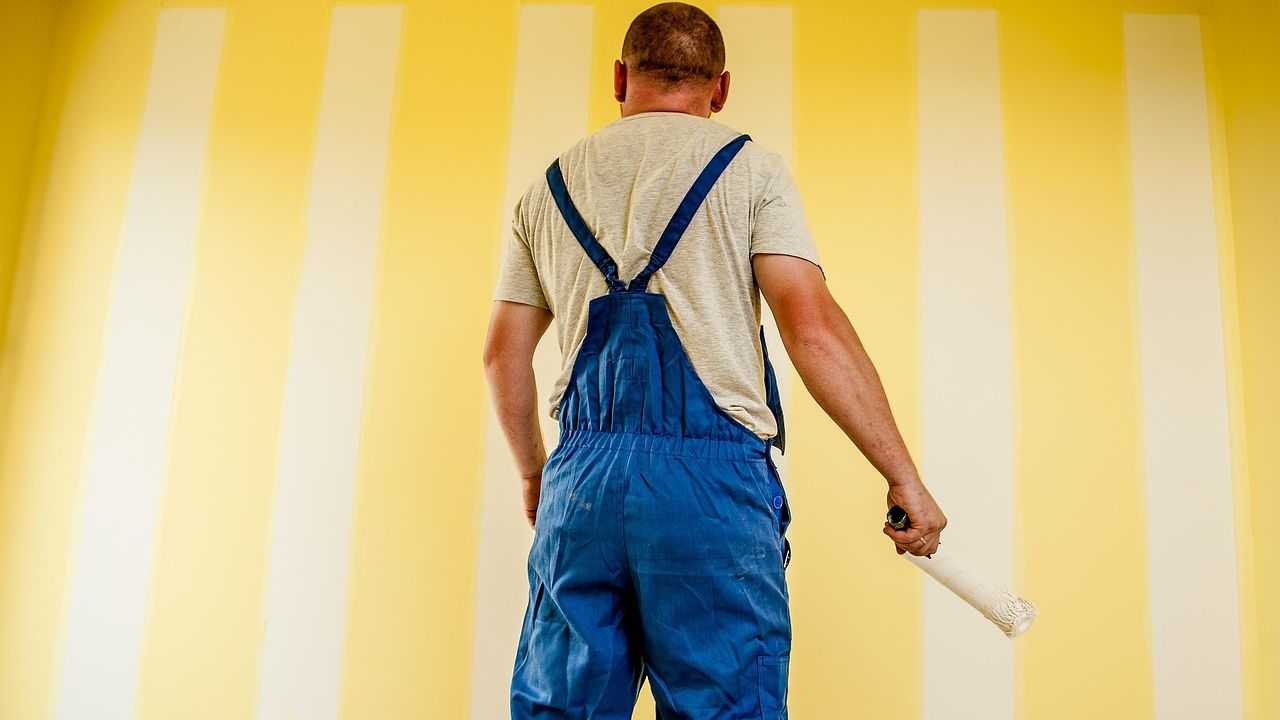 Decorator in overalls painting a yellow striped wall