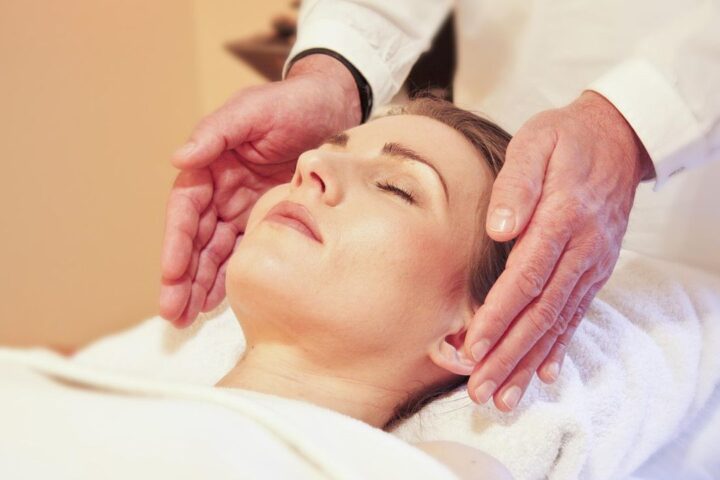 Healer resting hands beside the face of a relaxed woman with eyes closed