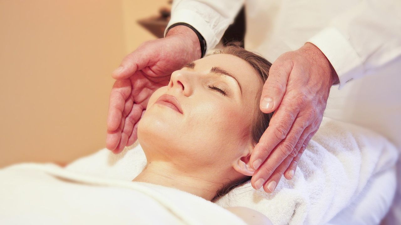 Healer resting hands beside the face of a relaxed woman with eyes closed