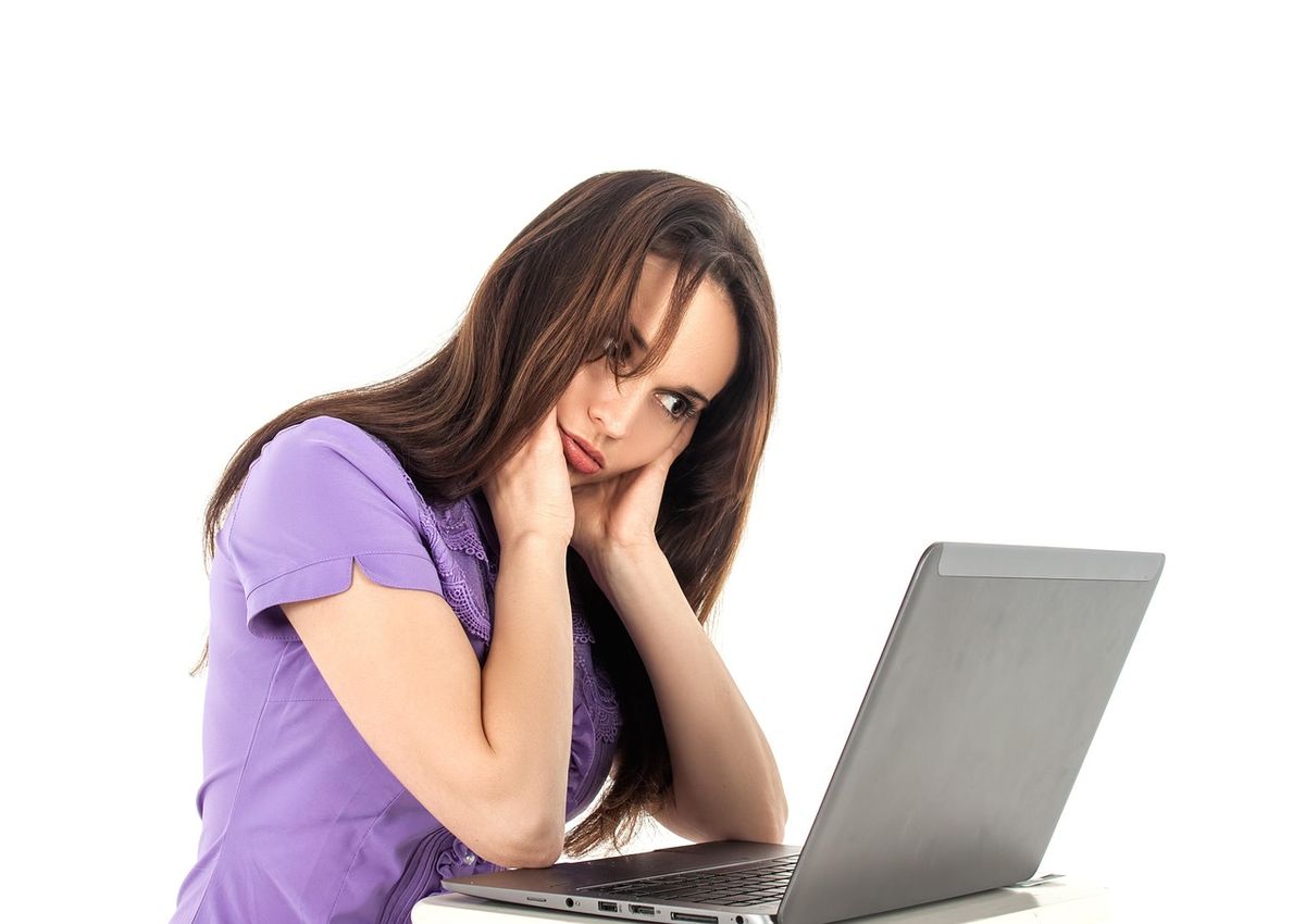 Tired young woman resting her head on her hands at a laptop