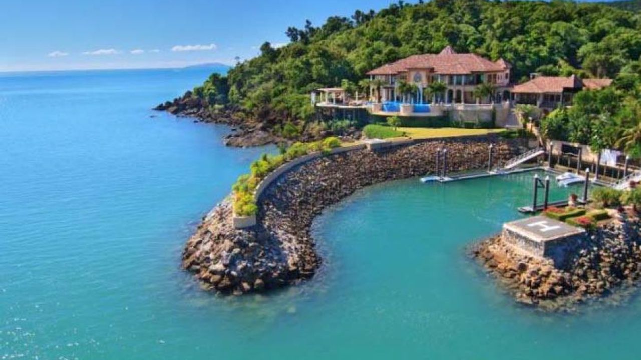 Aerial view of Mandalay House on a rocky headland by turquoise sea