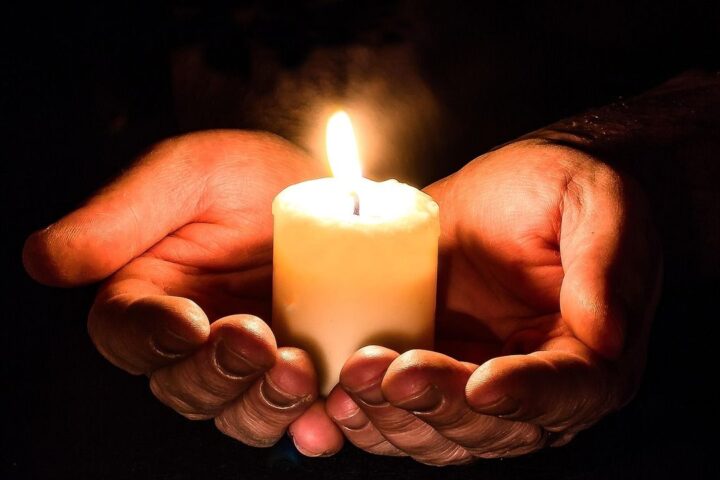 Cupped hands holding a lit candle in the dark