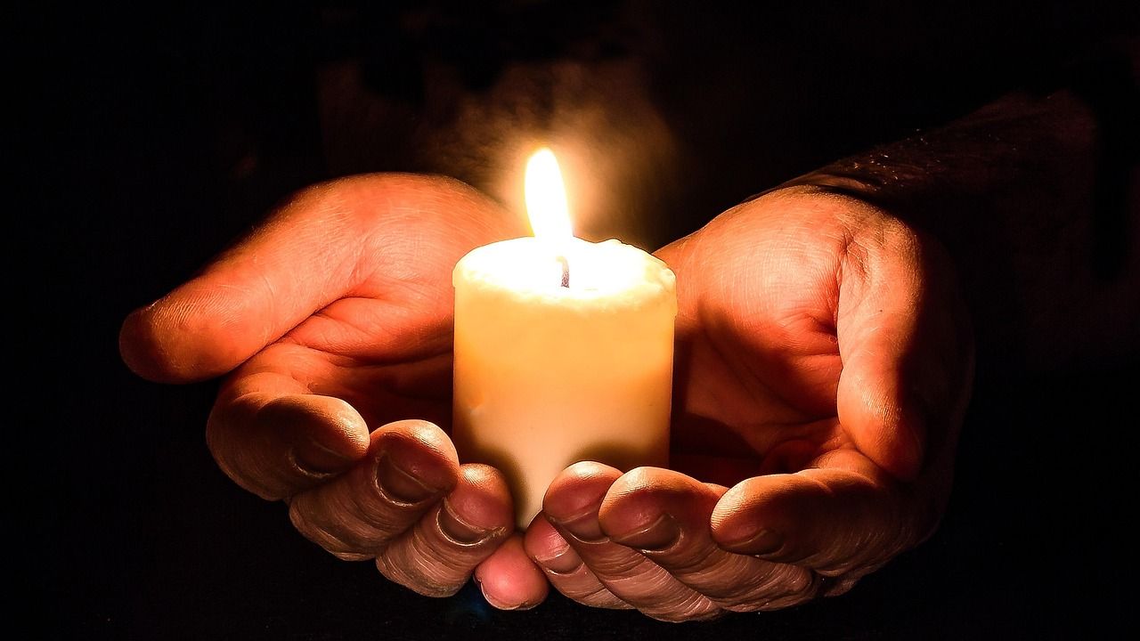 Cupped hands holding a lit candle in the dark