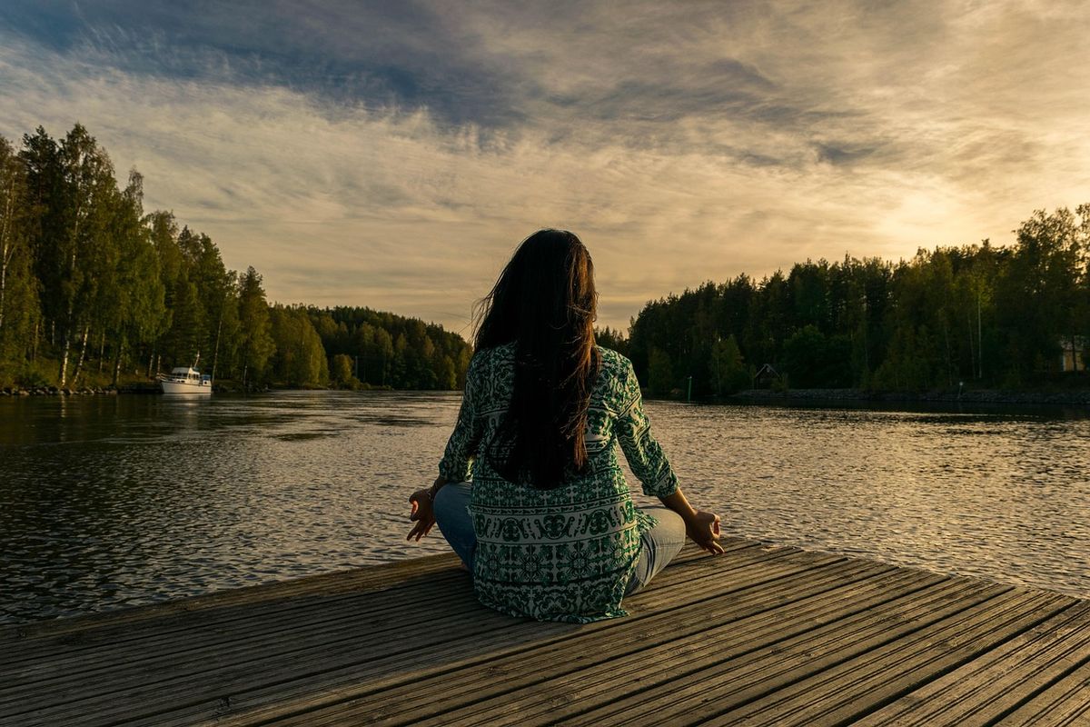 Woman meditating on a jetty by a lake at sunset