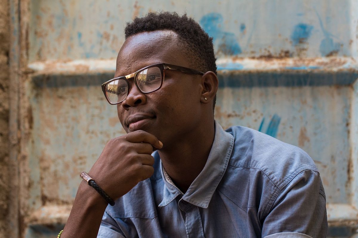 Thoughtful young man in glasses resting his chin on his hand