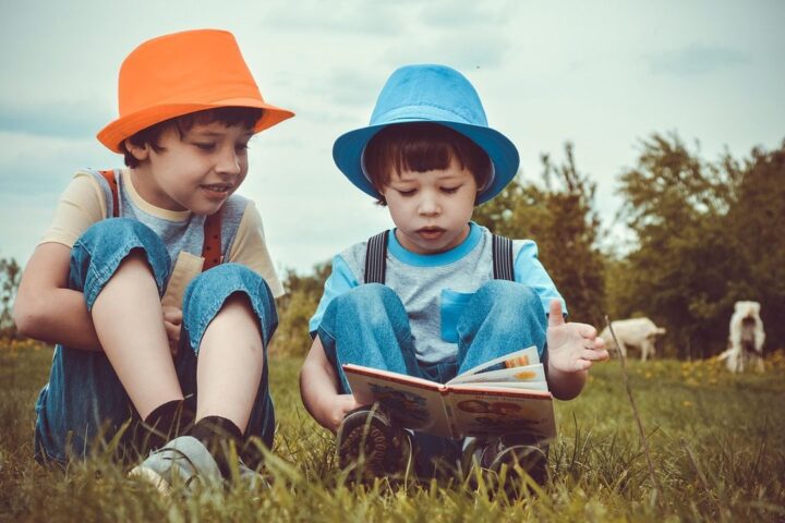 Two boys in colourful hats reading a book on the grass